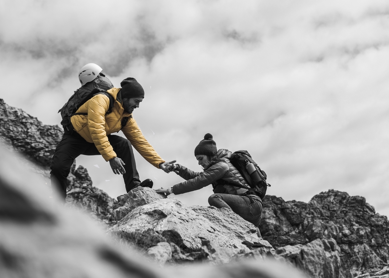 Climber helping another climber to the top of a rock slope